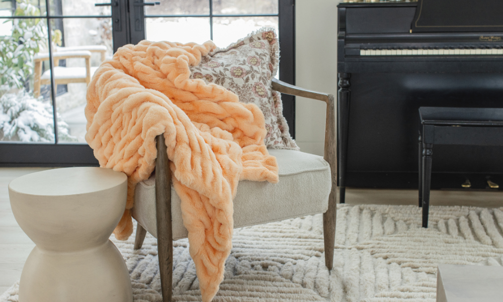 Passionate Peach Chic minky blanket from Minky Designs draped over a cozy accent chair beside a window, showing the blanket’s plush braided texture and inviting warmth.