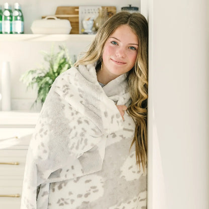 Woman wrapped in Arctic Lynx Posh Minky Blanket, smiling in cozy home setting