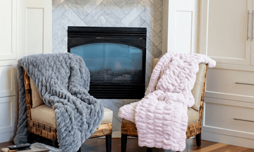Two chairs with fluffy minky blankets in front of a fireplace.