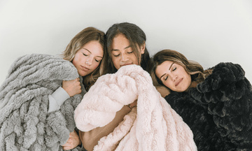 Three women wrapped in Minky Designs Chic blankets in Ash Gray, Blossom Pink, and Jaguar Black, highlighting the soft texture and luxurious feel of the Chic collection.