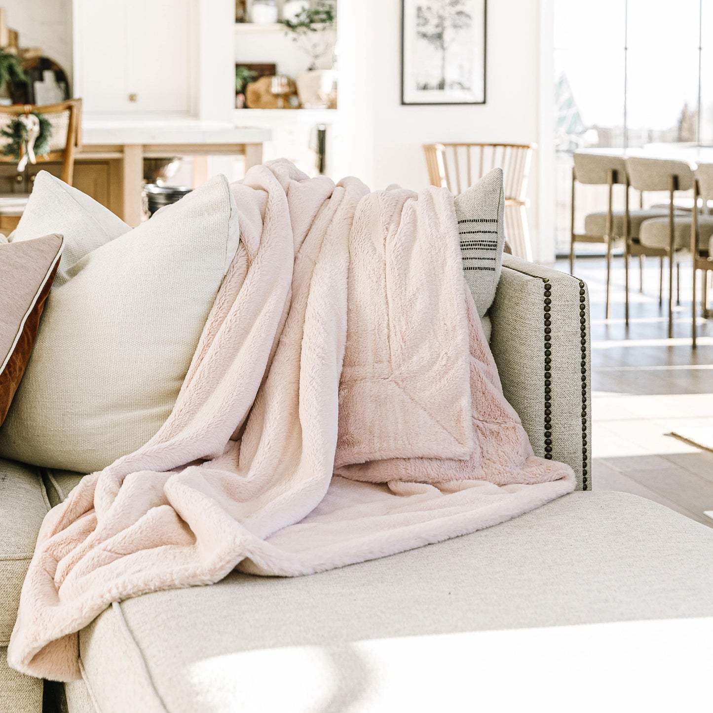 Blossom Pink Posh minky blanket from Minky Designs draped over a neutral sofa in a bright living room, showcasing its soft texture and elegant warmth.